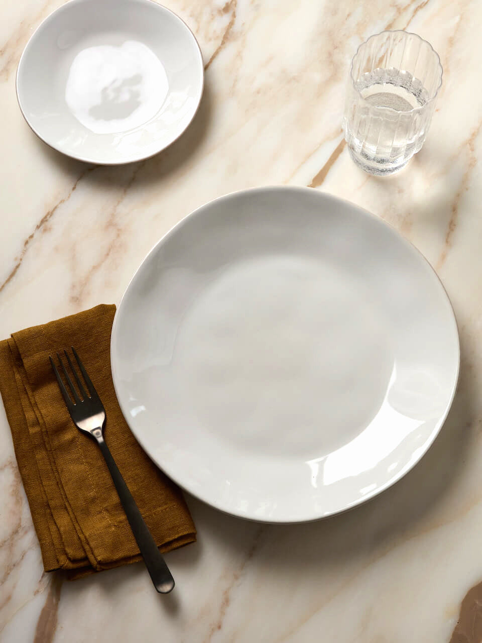 White ceramic plate on a marble surface with a fork and glass of water.