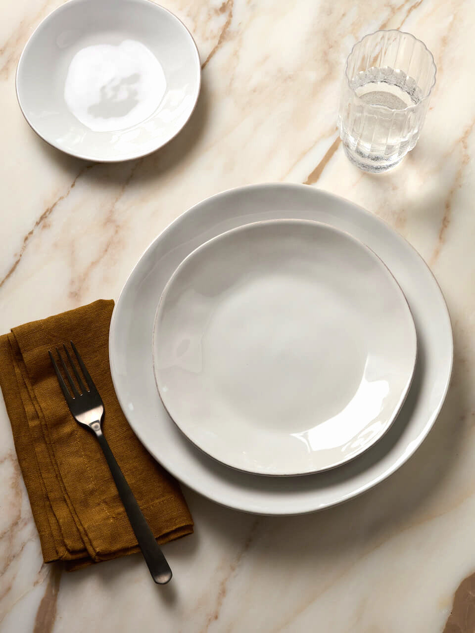 White ceramic plates on a marble surface with a fork and napkin.