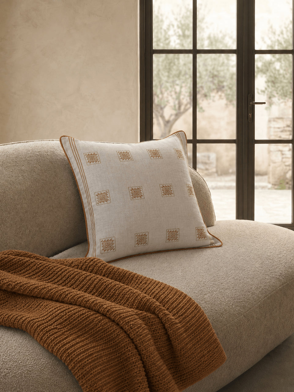 Luxury cream and caramel patterned cotton cushion cover with woven geometric detailing, styled on a textured boucle armchair in a warm contemporary interior.