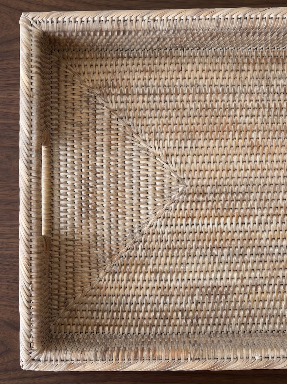 Overhead close-up of a rectangular handwoven rattan tray with integrated handles placed on a dark walnut coffee table against a textured cream rug.