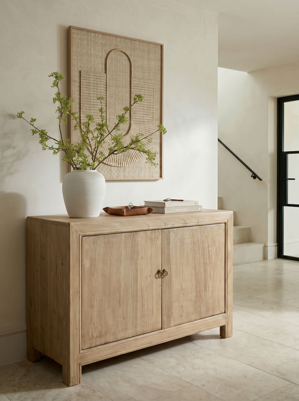 Wooden sideboard with a vase of greenery and framed artwork in a room.