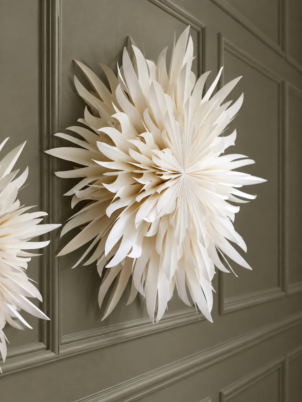 Large cream paper swowflake wall decor hanging on a dark gray paneled door, with a second partial flower visible at the left edge.