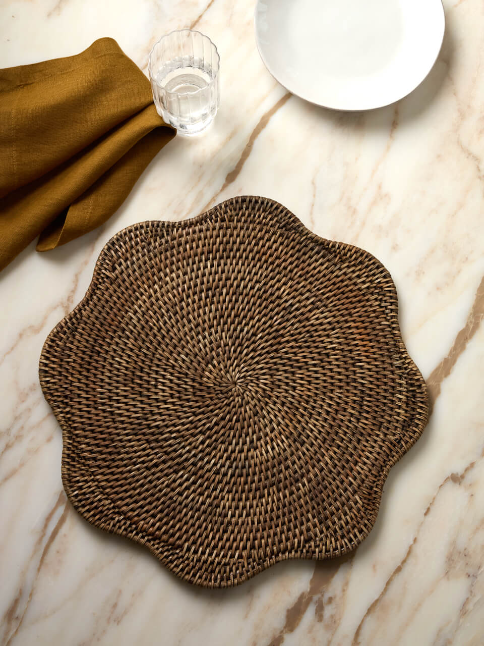 Ayre scalloped rattan placemat in antique brown on marble table with linen napkin and glassware
