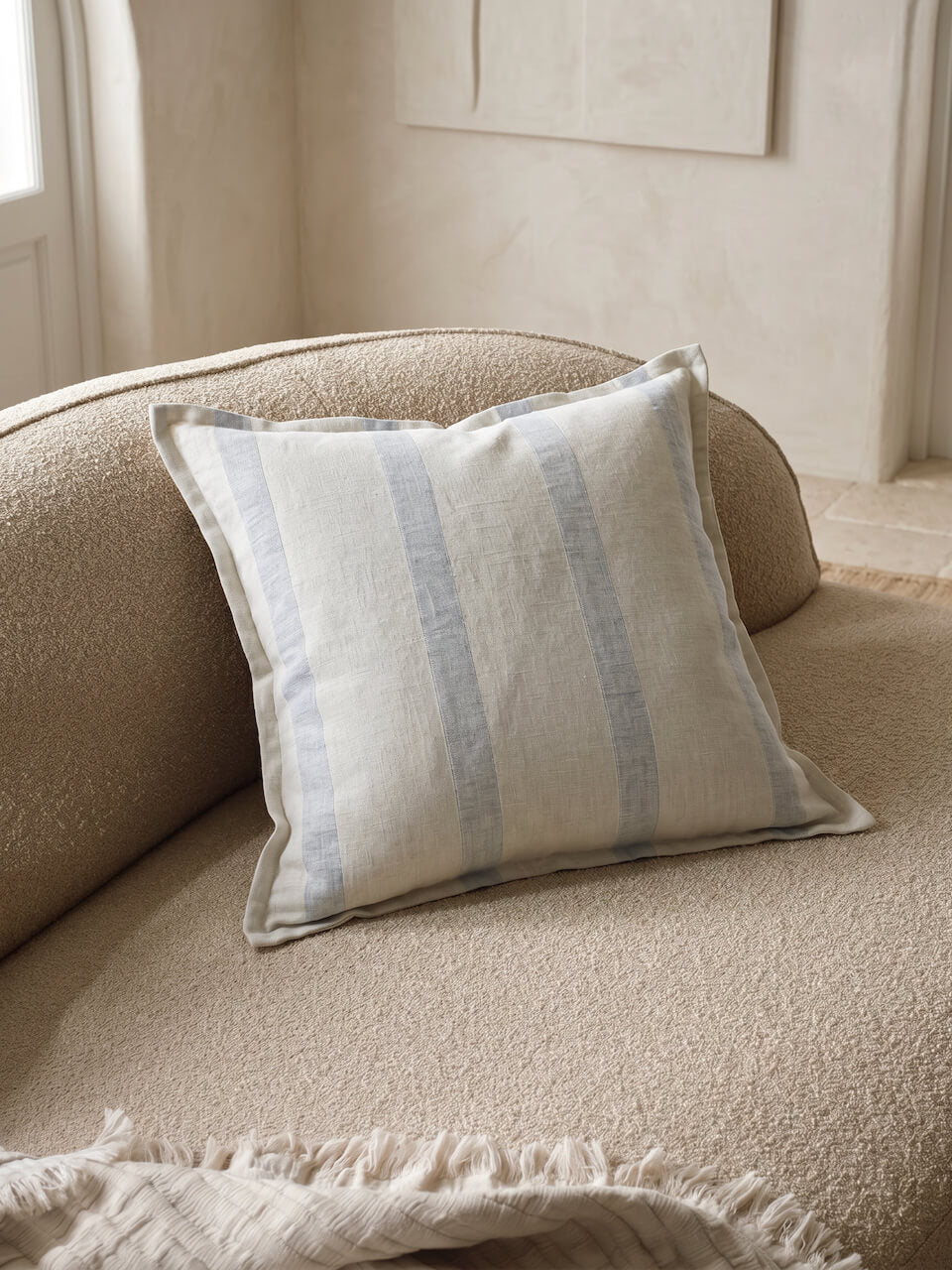 Luxury blue fog striped cotton linen cushion cover styled on a textured neutral boucle armchair in a soft contemporary interior.
