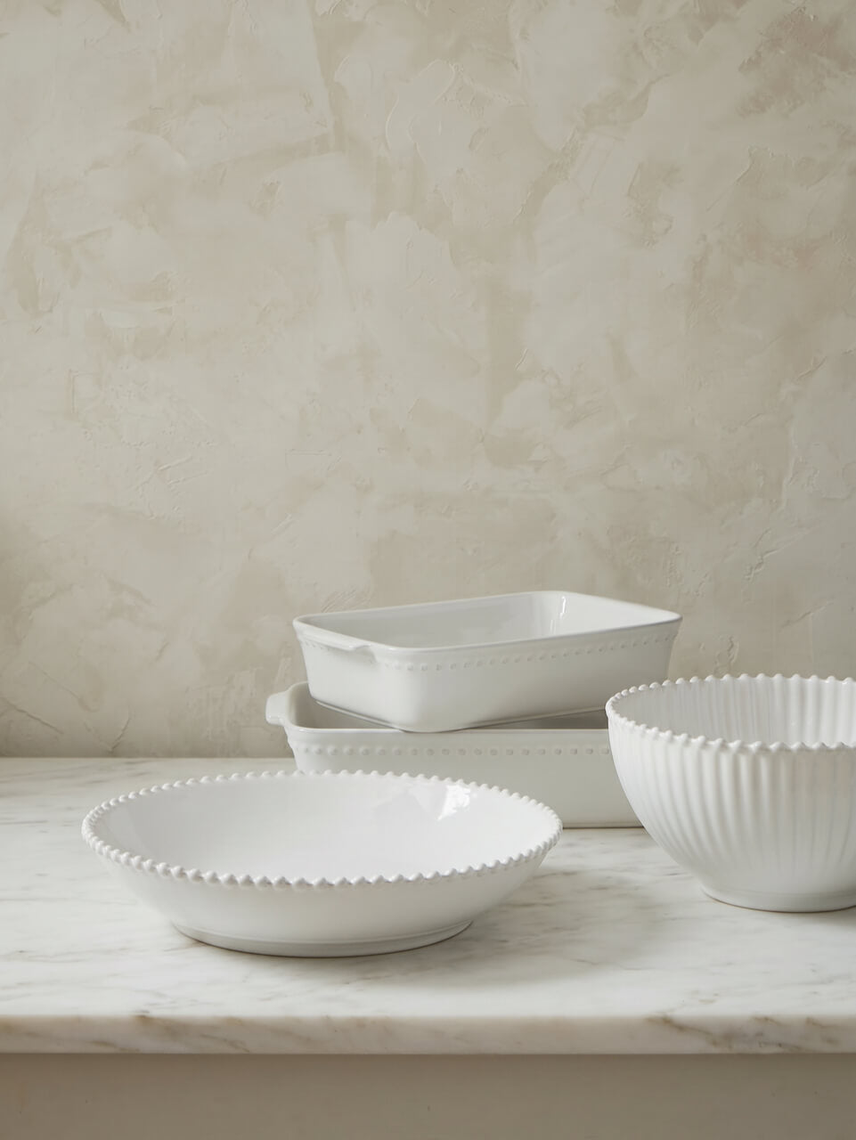 Set of white ceramic dishes on a marble surface with a beige textured wall background