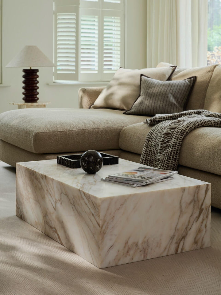 Beige sectional sofa with a marble coffee table in a living room setting.