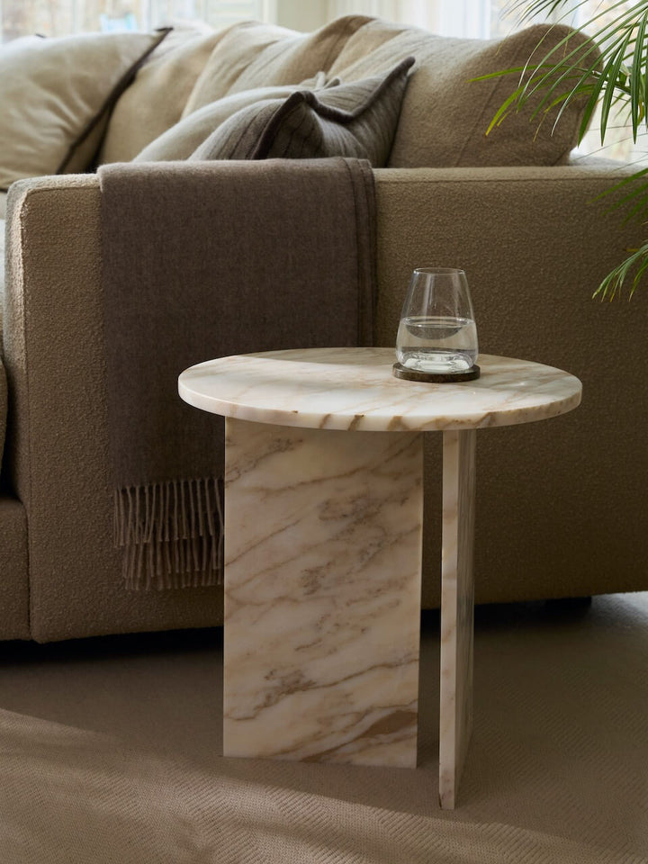 Marble side table with a glass of water in front of a beige sofa.