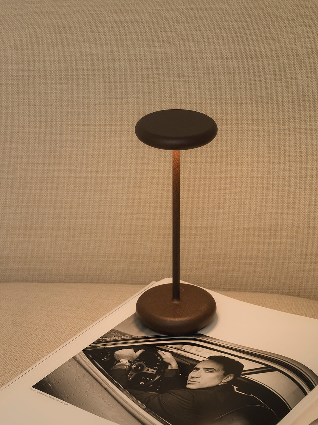 Close-up of Lana corten rechargeable table lamp showing slim minimalist design and warm indirect glow cordless dimmable lighting on magazine