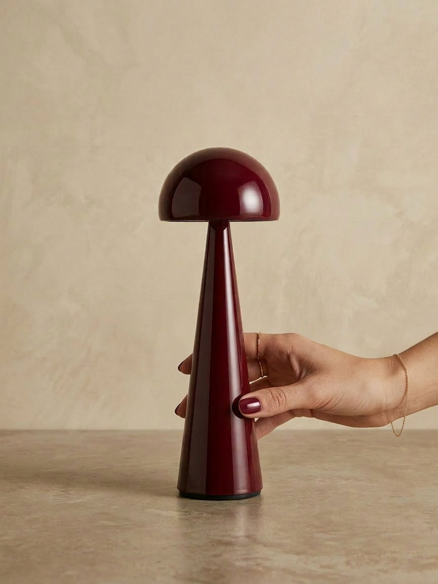 Zanzi rechargeable table lamp in burgundy lacquer held in hand showing size and glossy mushroom design cordless dimmable warm light lamp