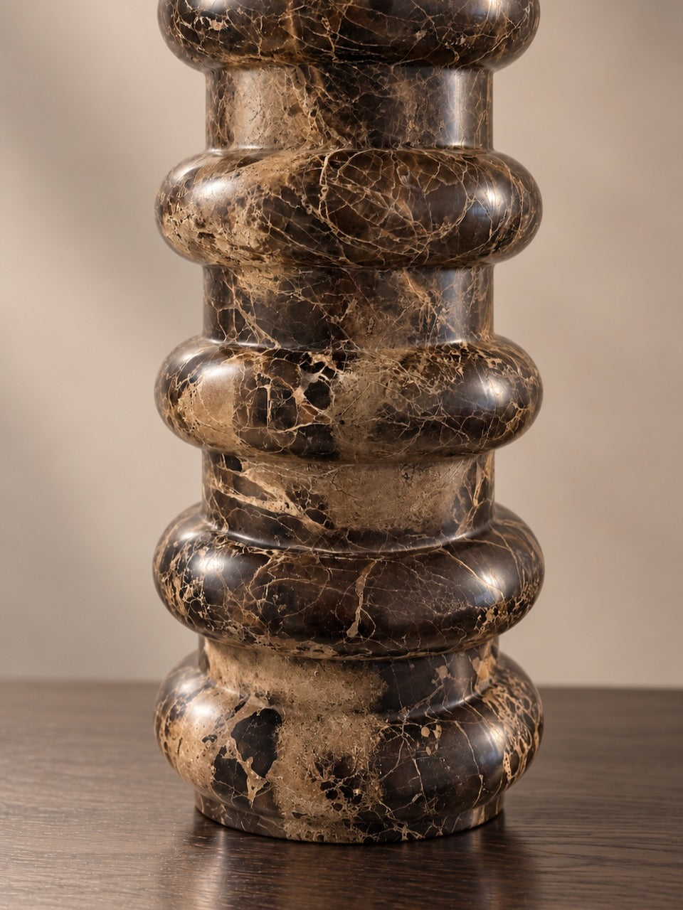 A close-up of a dark brown and black marble table lamp with elegant gold veining, featuring a stacked, ribbed design on a wooden surface against a neutral beige background.