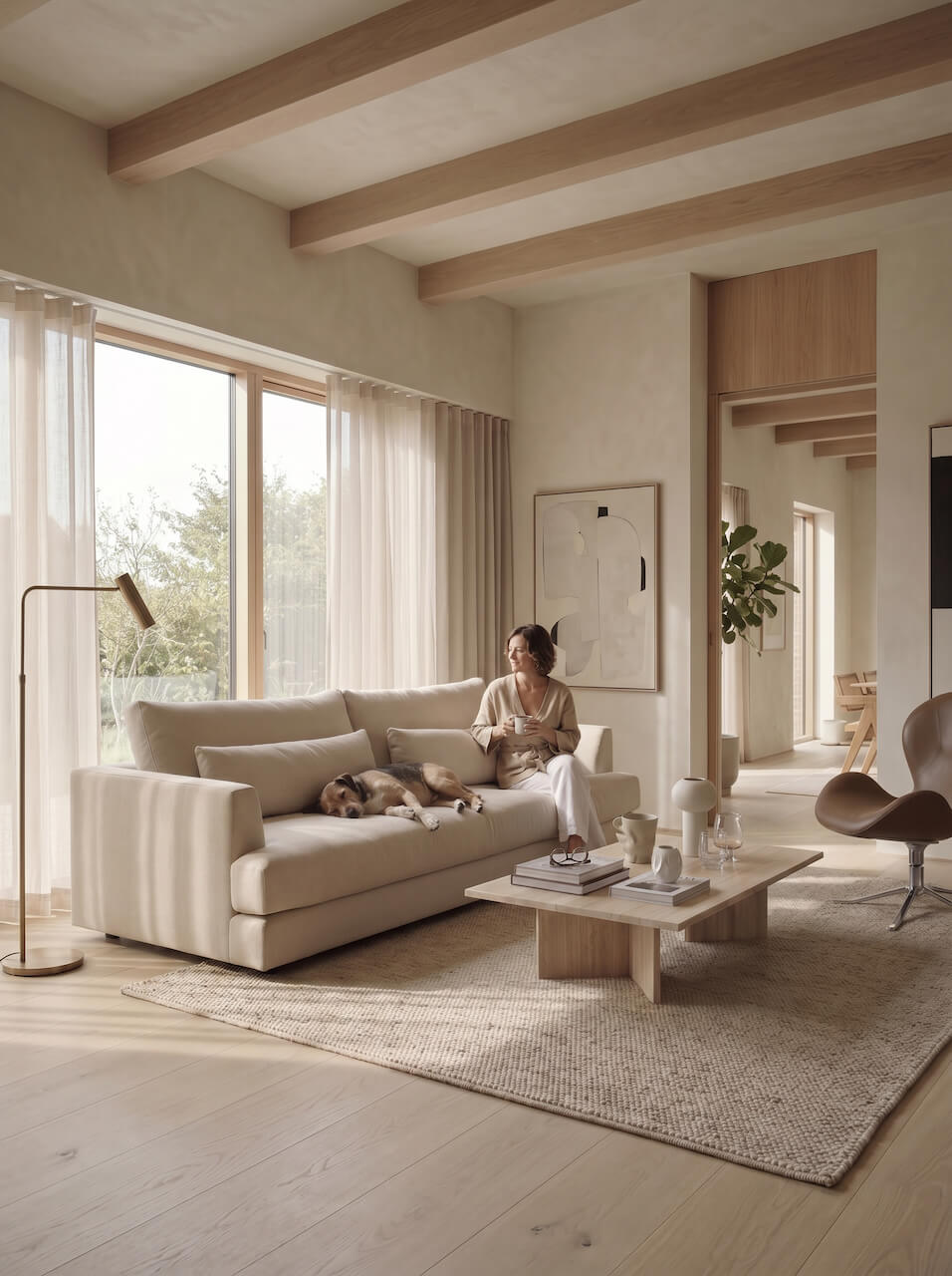 Woman sitting on a couch with a dog in a modern living room with large windows and wooden beams.